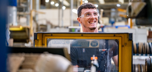 White male factory worker at factory machinery, with glass panel infront of body