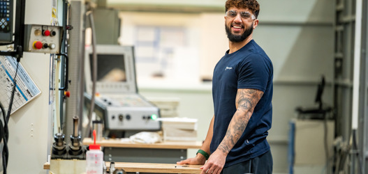 Male factory worker wearing blue t-shirt, with arms holding on to bench of factory machinery