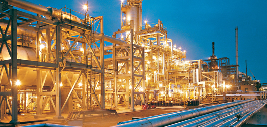 Illuminated oil refinery with grey pipes in the foreground