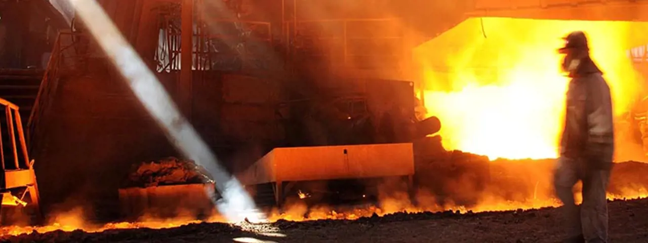 Person wearing fireproof clothing and helmet in foreground of molten metals factory