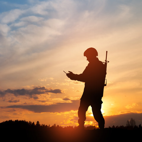 Soldier with drone control in their hands, with a forest in the distance and sunset with orange sky above