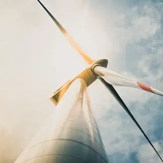 White and red wind turbine tower and blades taken from the base of the tower with cloudy blue sky in background