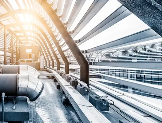 Scene of grey industrial pipes on top of building, encased by metal building structure in the shape of an arch.