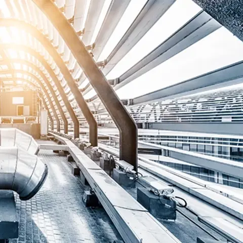 Scene of grey industrial pipes on top of building, encased by metal building structure in the shape of an arch.