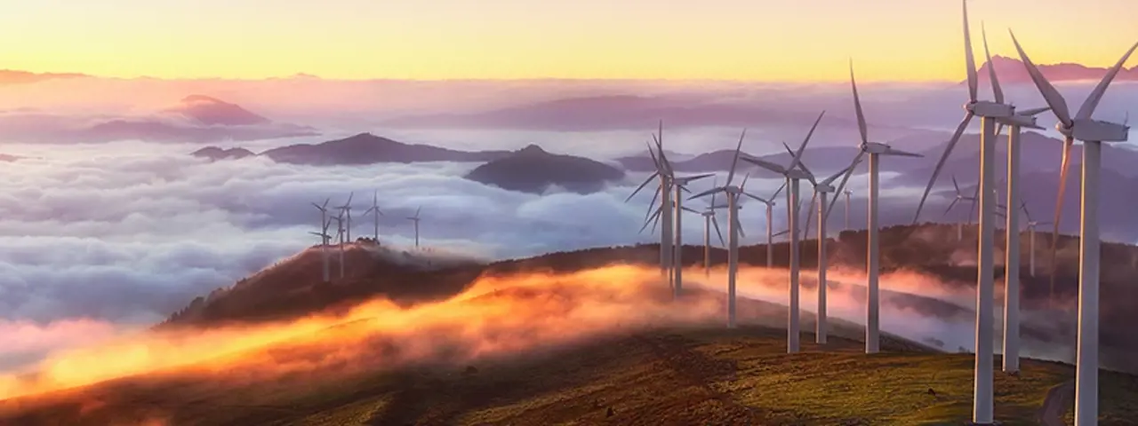 Row of wind turbines on mountain top above the clouds with a sunset background