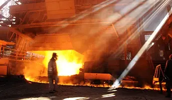 A molten metals worker walking across a factory infront of an open furnace door