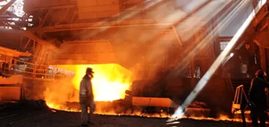 A molten metals worker walking across a factory infront of an open furnace door